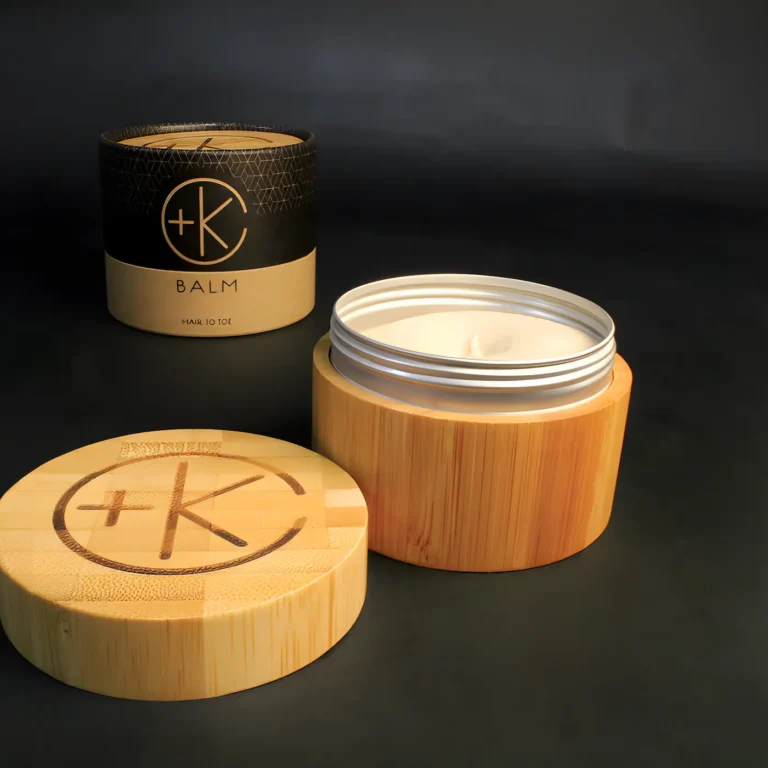 a bamboo container with a c+k logo on the lid and a circular cardboard packaging displayed in the back. a smooth cream is in the pot.