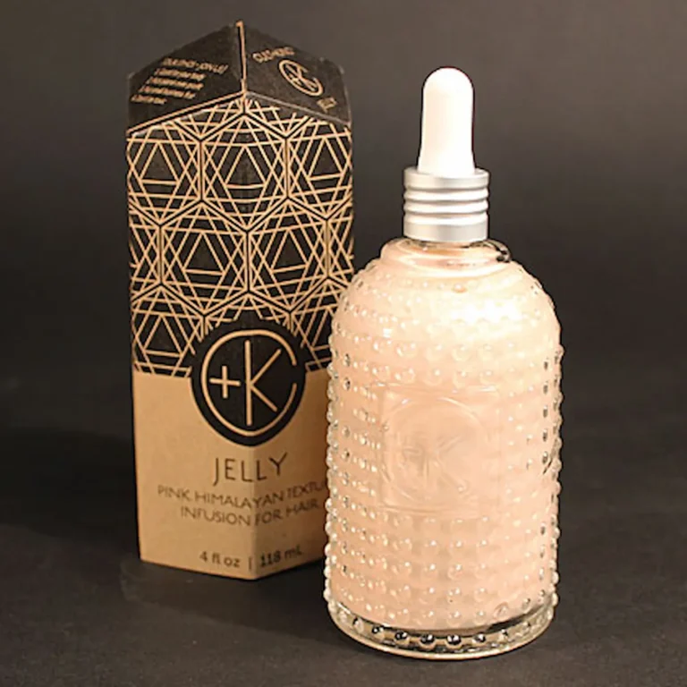 a glass bottle has a light pink cream inside. there is a white squeezer dropper and a cardboard obelisk packaging with sacred geometry.