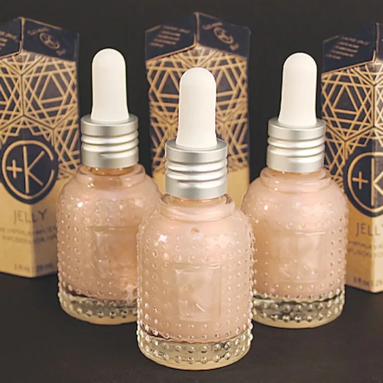 3 cutie lil glass bottles with white squeezer tops for droppers, clear glass bottles show a pink serum with cardboard packaging in the background.