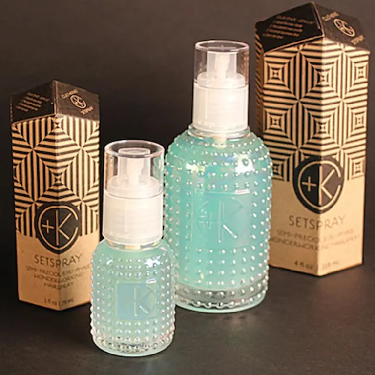 a full size and a mini bottle shows a malachite colored liquid and each glass bottle has a white spray lid and cardboard obelisk packaging.