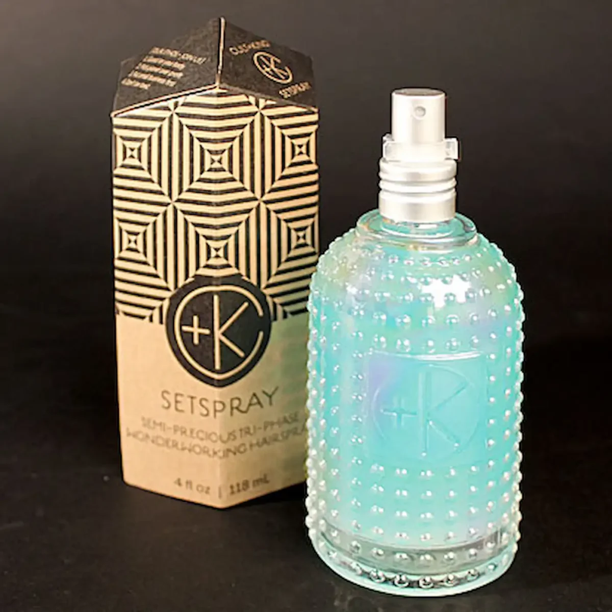 a glass bottle with a white spray lid and a malachite colored fluid inside stands in front of an obelisk cardboard package.
