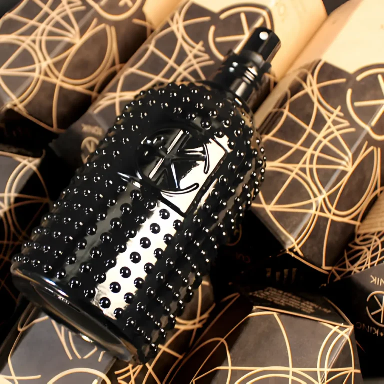 a black glass bottle with glass dots and a black sprayer with a lid on it sits on a black background in front of it's obelisk cardboard packaging.