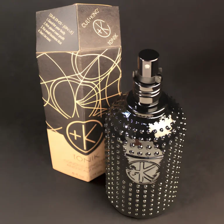 a black glass bottle with glass dots and a black sprayer with a lid on it sits on a black background in front of it's obelisk cardboard packaging.