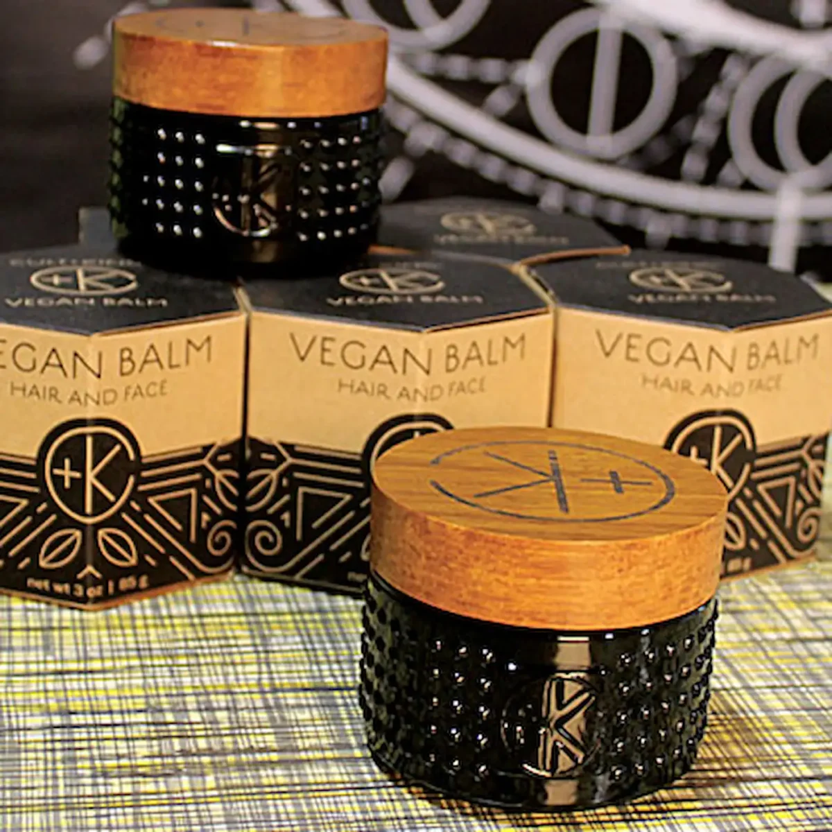 a cute tiny black glass jar with a bamboo like and a black c+k logo. there are geometric cardboard boxes behind it and another lil jar.