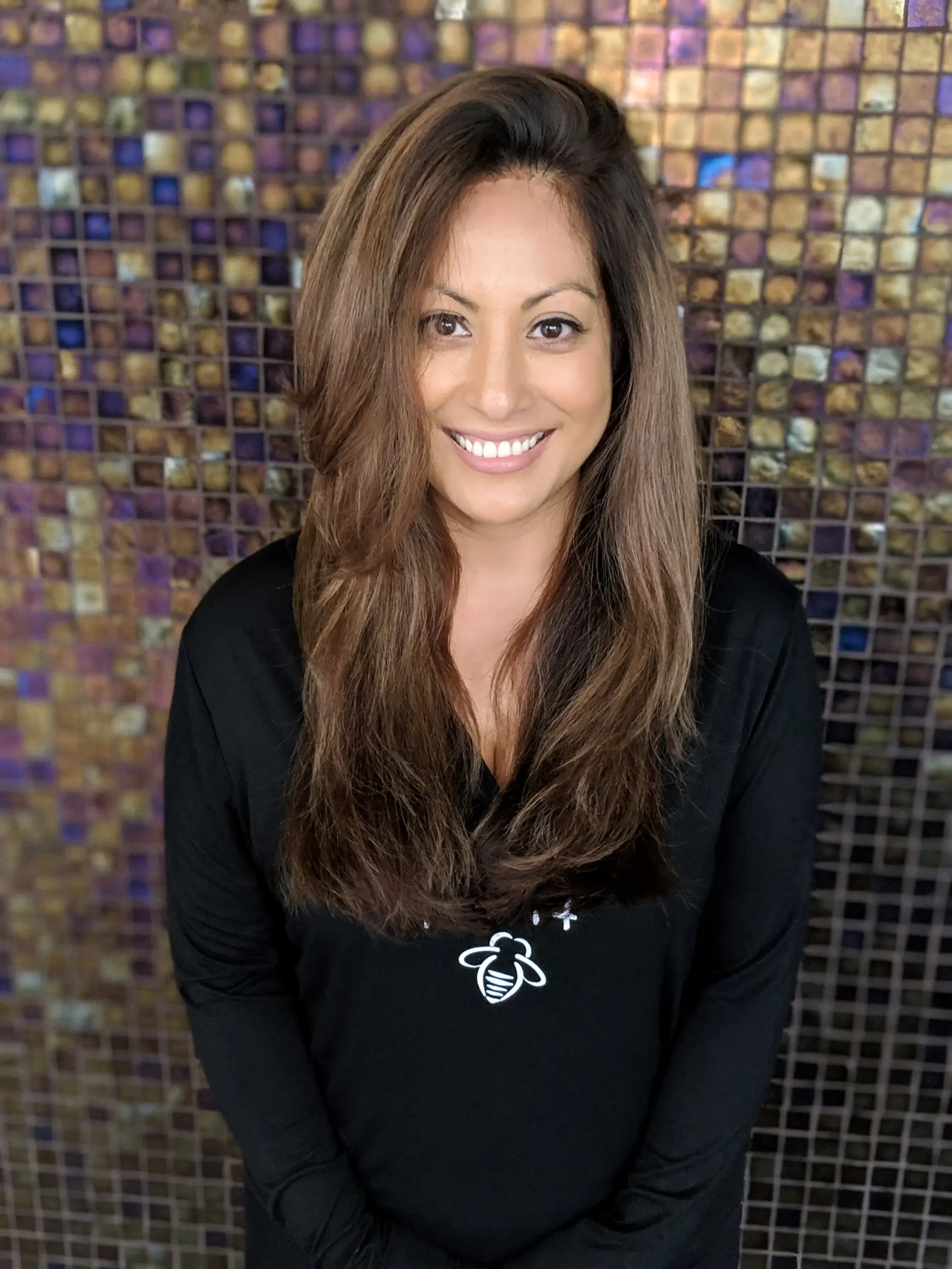 a woman with grey coverage and caramel brunette highlights and balayage stands in front of a mosaic background