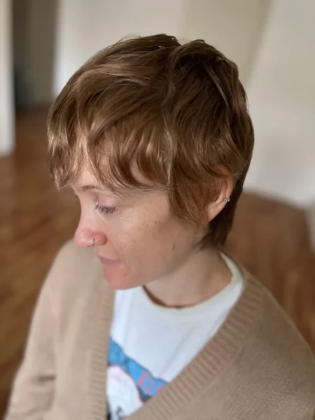 a woman with sandy warm blonde hair looks away and is wearing a white shirt and a beige cardigan