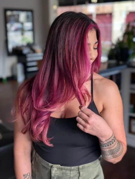 Long layered haircut with vivid pink balayage and babylights, smooth blowout, side angle view.