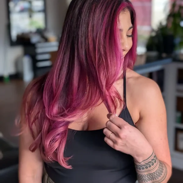 Long layered haircut with vivid pink balayage and babylights, smooth blowout, side angle view.