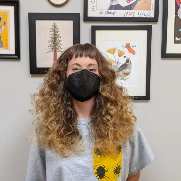 Long curly haircut with natural volume and textured fringe, brunette with golden highlights, front view.