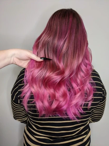 Long vivid pink balayage with dimensional waves, stylist’s hand showing detail, back view.