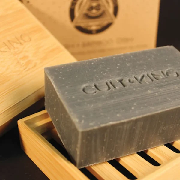 Cult+King charcoal Wash bar on bamboo soap dish with embossed branding, angled view.