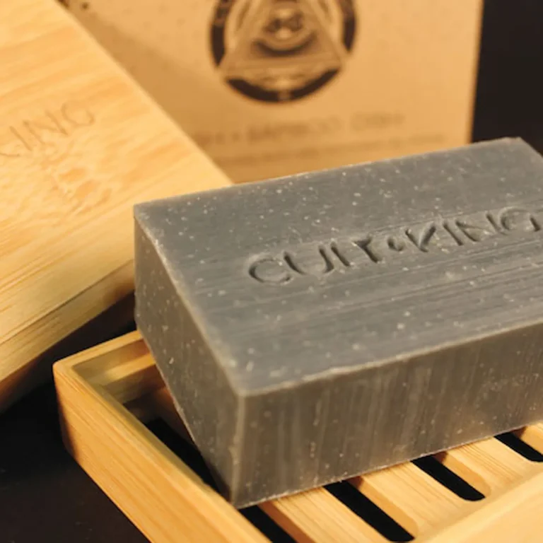 Cult+King charcoal Wash bar on bamboo soap dish with embossed branding, angled view.
