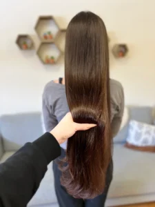 Extra long brunette hair with glossy finish and soft ends, stylist’s hand showing length, back view.