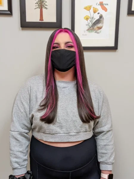 Sleek brunette hair with bold pink money piece highlights, straight finish, front view.