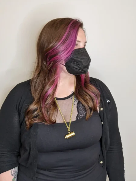 Brunette long layers with vivid pink money piece and soft curls, side angle view.