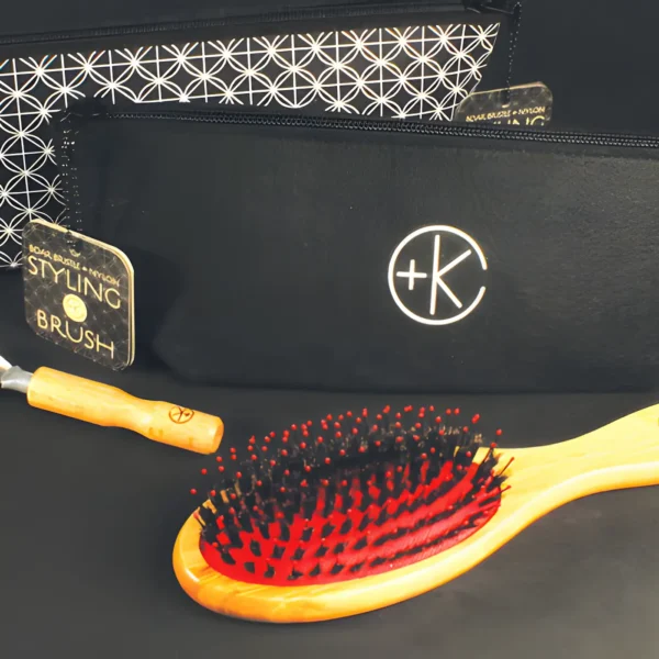 a red pad on a bamboo boar bristle brush sits in front of it's black felt carrying bag and cleaning rake.