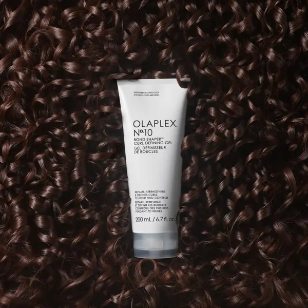 Olaplex No. 10 Bond Shaper curl defining gel on dark brown curly hair background.