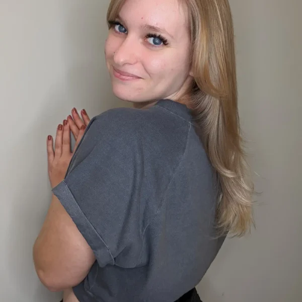 Warm blonde long-layer haircut with face-framing and soft blowout, back three-quarter view.