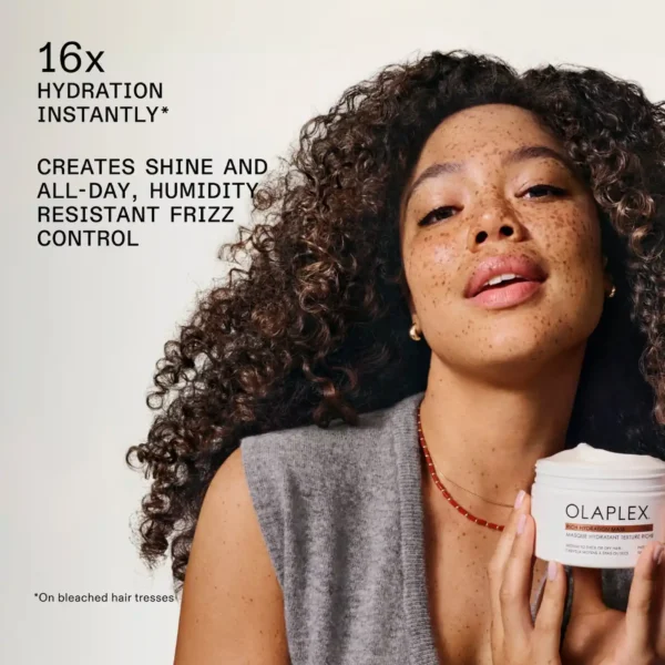 A woman with beautiful, defined curly hair holding the Olaplex Rich Hydration Mask jar. The product promises 16x hydration and all-day humidity-resistant frizz control.
