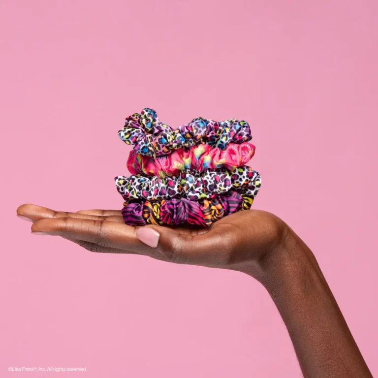 a hand holds 4 ruched scrunchies in various rainbow colors with a pink background