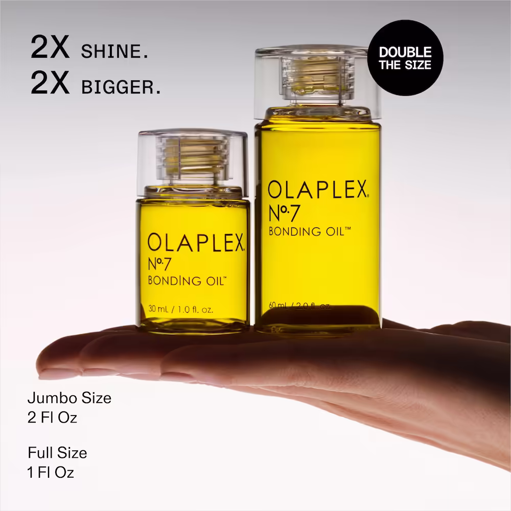a hand holds two bottles of golden olaplex oil the original 1 oz and a 2 oz jumbo size of the bonding oil