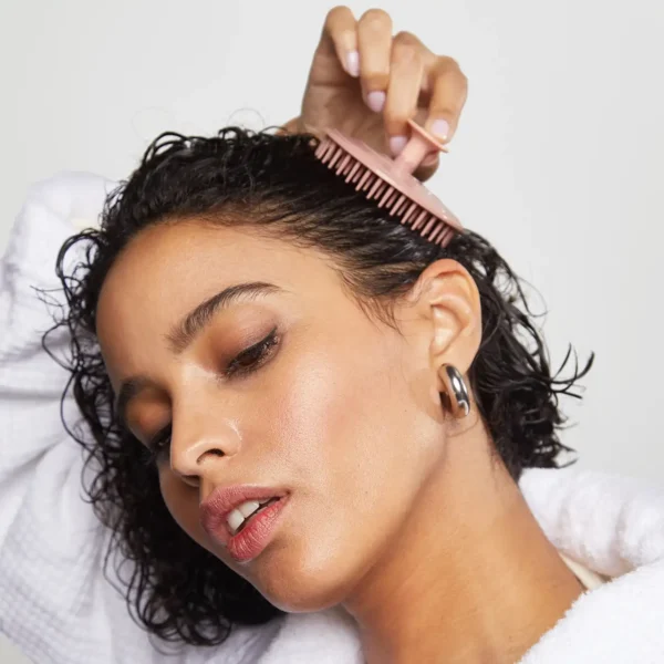 a woman with short brown hair uses her scalp braush to massage her scalp