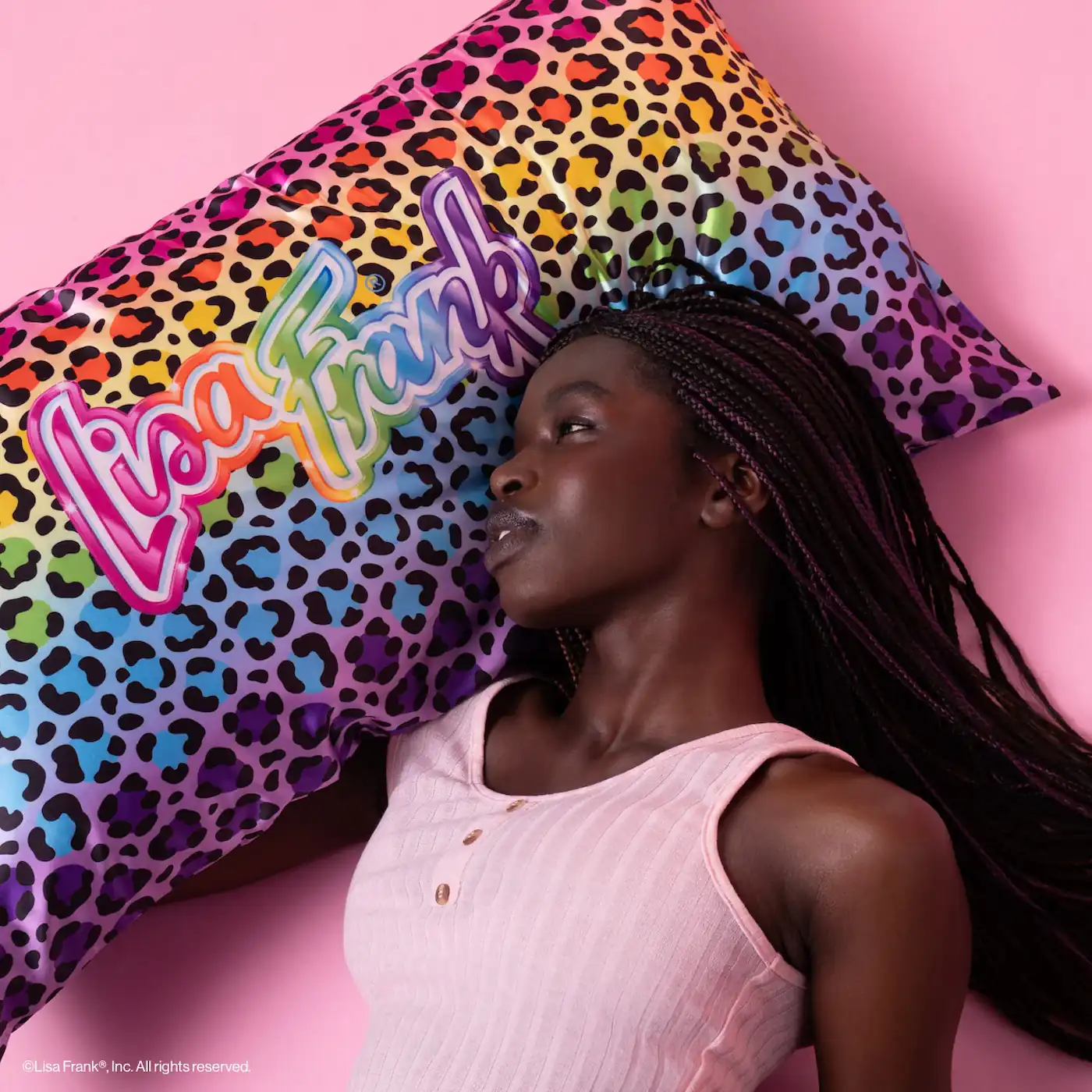 a woman stands in front of a pnk backdrop ans she holds her king sized pillow with a rainbow leopard lisa frank logo