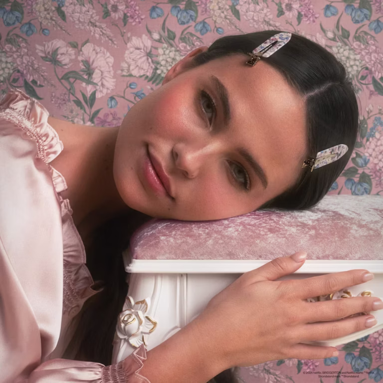 a woman rests her weary bones on a stool while she models her creaseless clips in front of a floral wallpaper