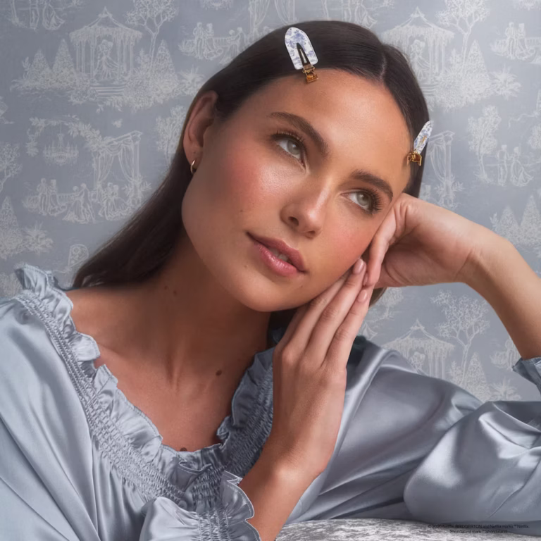 a woman looks off in the distance wearing the bridgerton x kitsch creaseless clips in front of a pale blue wallpaper