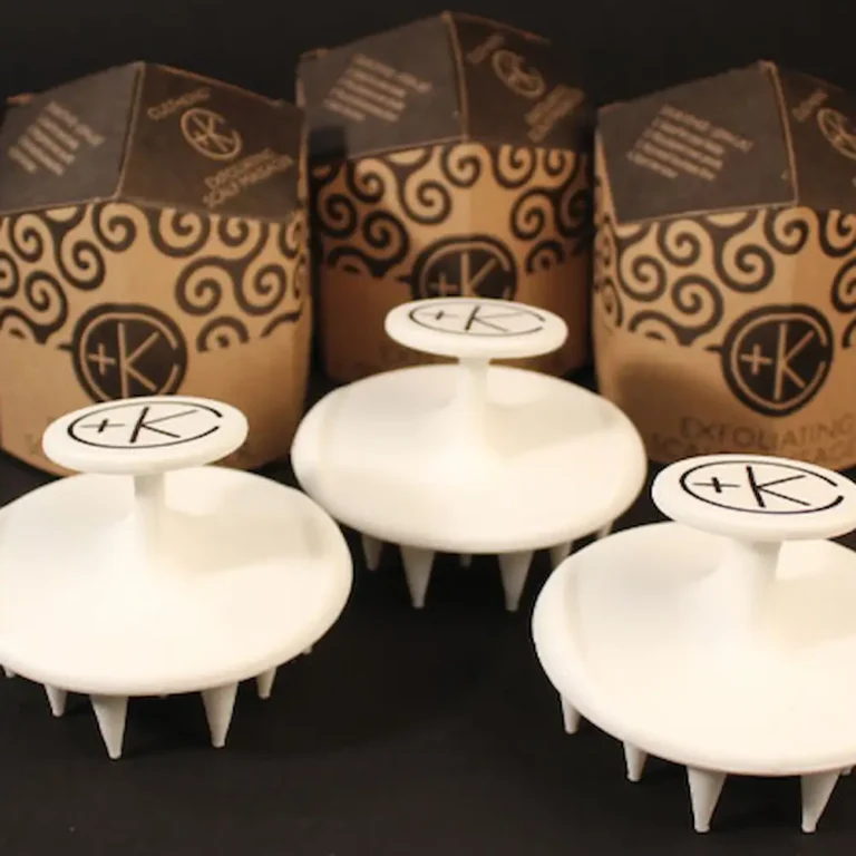 3 white silicone scalp massagers sit in fron tof their obelisk cardboard and sacred geometry packaging from cult + king