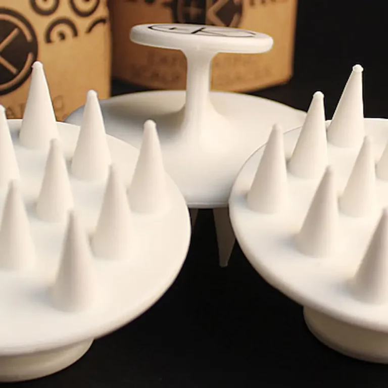 a close up of the white sillicone scalp massager from cult + king showing tapered teeth for exfoliating and massaging the scalp