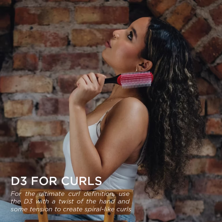 A person with long, defined curls holding a classic Denman D3 styling brush. Text overlay explains how to use the brush with tension and a twist of the hand for spiral-like curls.